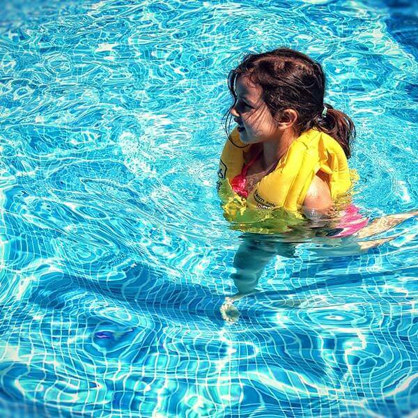 A child with brown hair and a yellow life jacket swims in a pool.
